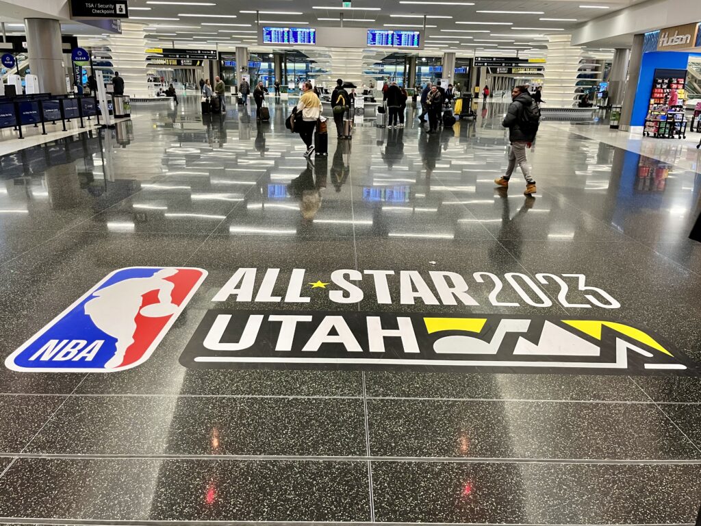 A photo of an airport ticketing area with a large NBA graphic on the ground